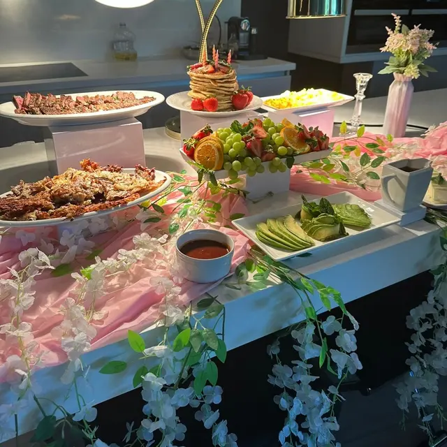 Pink-themed brunch buffet — pancake stack, fresh fruit, and florals under gold lamps